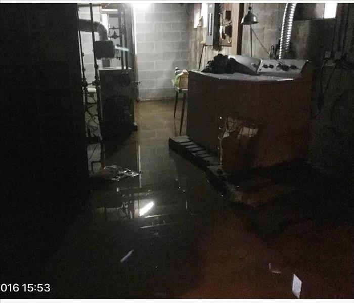 Concrete basement with inches on water on the floor around washer/dryer on pallets, and furnace