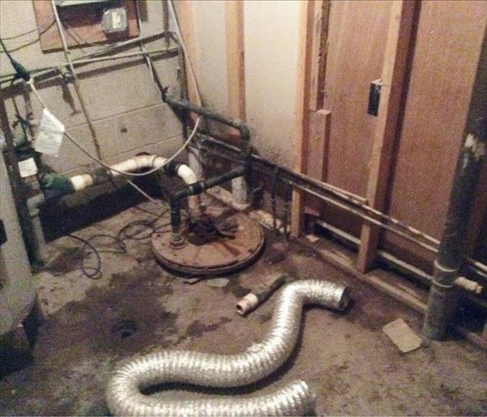 Piles of mud and debris and a vent hose on the floor around a sump pump in a concrete room