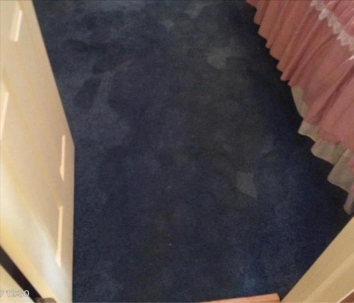 Blue saturated carpet with wet footprints by a pink bed skirt