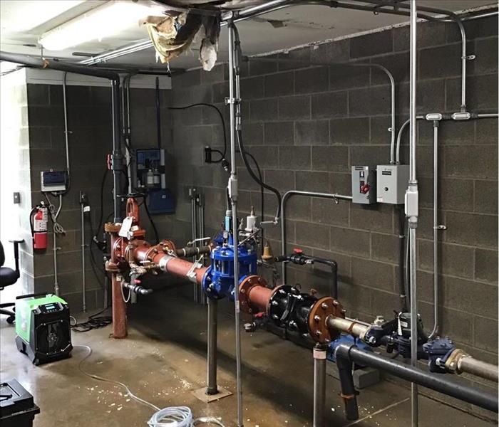 Pipes running through a room with water and debris all over the floor